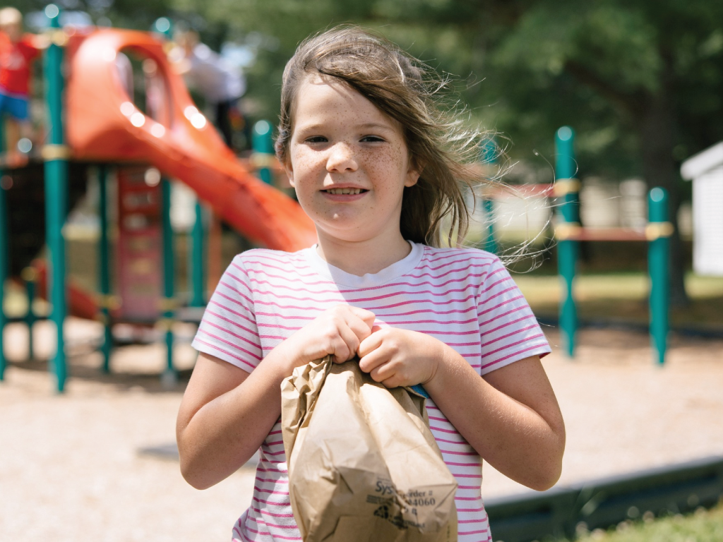 Young girl holding back outside by school playground. 